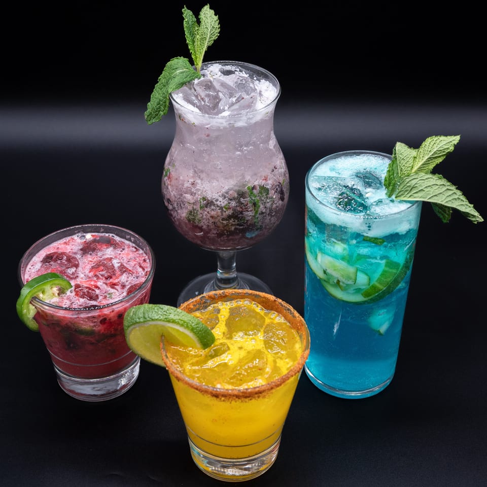Four vibrant Ambrosia Zaika cocktails: red with jalapeño, purple with mint, yellow with chili-lime rim, and blue with mint.