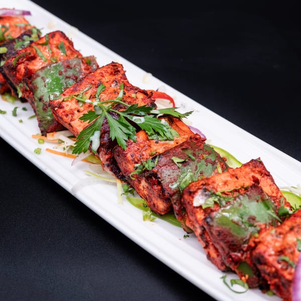 Spicy paneer tikka skewers with green bell peppers and cilantro on a white platter.