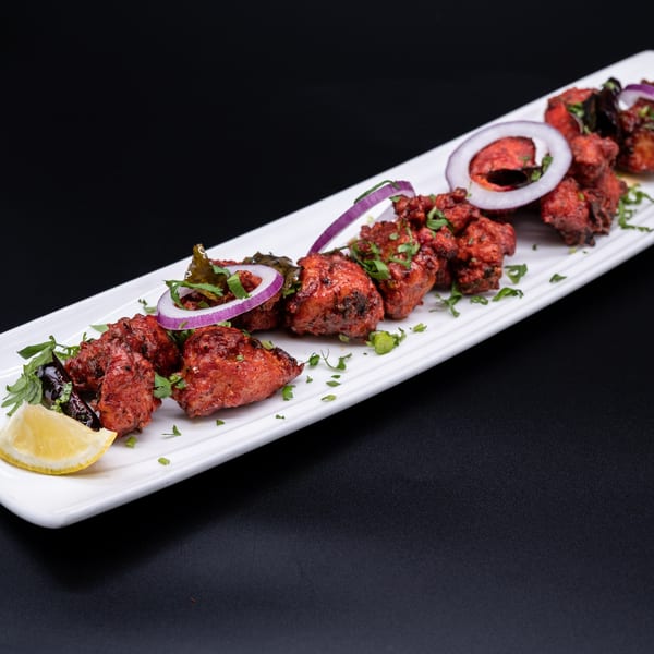 Ambrosia Zaika's red Indian chicken tikka, garnished with onions, cilantro, and a lemon wedge.