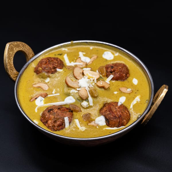 Ambrosia Zaika's Malai Kofta, a rich Indian curry with vegetable dumplings, nuts, and cream in a brass bowl.
