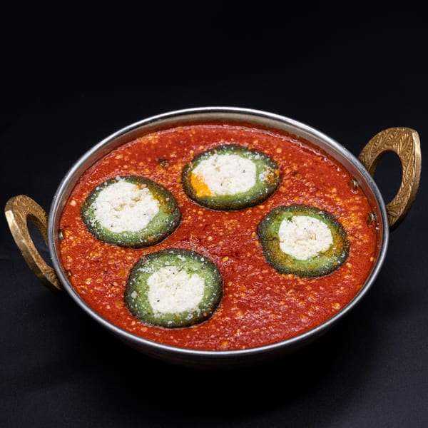 Indian dish with four green and white stuffed kofta in a rich red tomato gravy, served in a brass karahi.