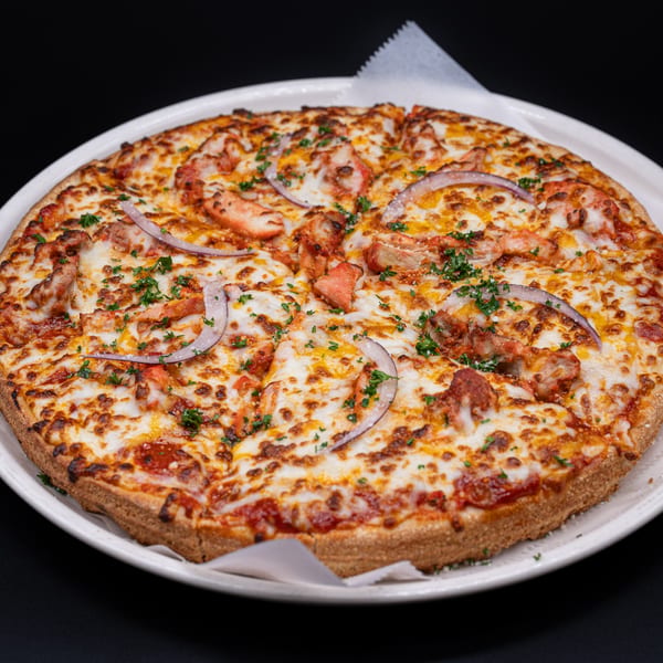 A whole Ambrosia Zaika Indian pizza, topped with chicken, red onions, cheese, and parsley.