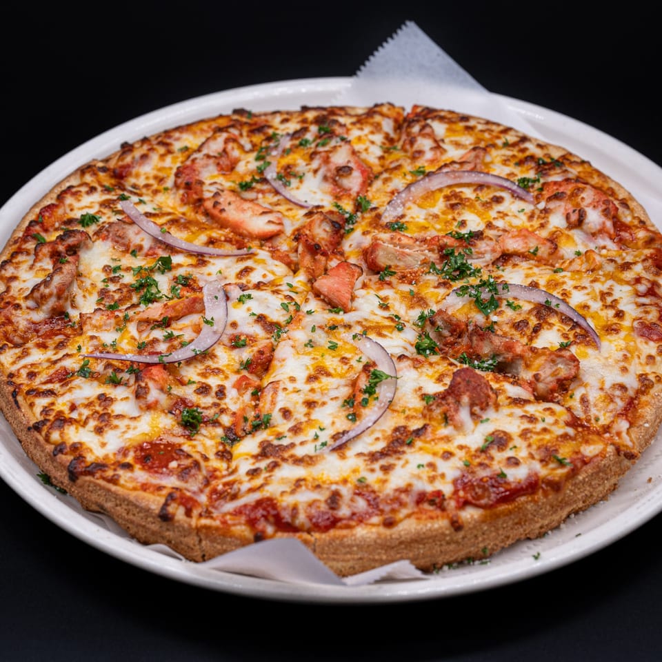 A whole Ambrosia Zaika Indian pizza, topped with chicken, red onions, cheese, and parsley.