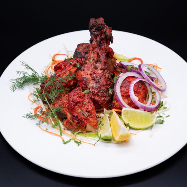 Ambrosia Zaika's Indian Tandoori Chicken, garnished with red onions, lime, and fresh dill on a white plate.