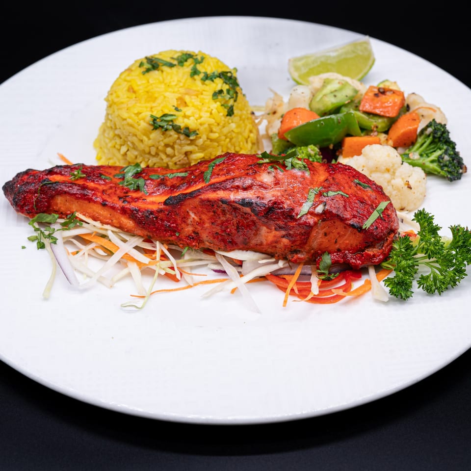 Tandoori salmon with yellow rice, mixed vegetables, and a lime wedge on a white plate.