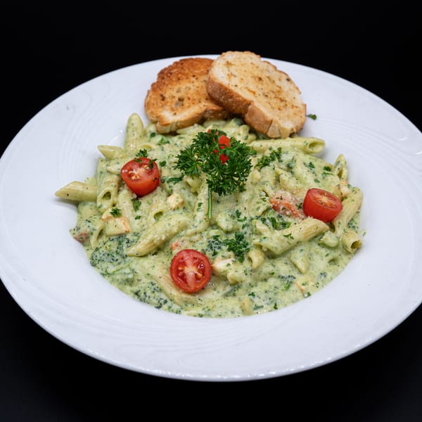 Creamy green pasta with penne, cherry tomatoes, and parsley, served with two slices of garlic bread.